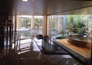 Ein moderner Poolbereich im Innenbereich mit Glaswänden, einer Holzterrasse und Blick auf eine natürliche Landschaft.
