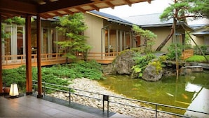 Um jardim japonês tradicional com lago de carpas, pontes de madeira e um farol de pedra.