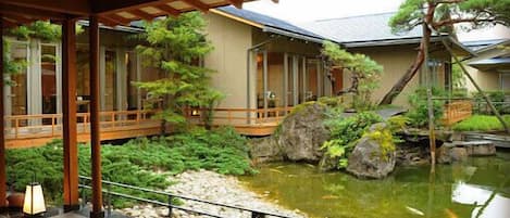 Un jardín tradicional japonés con un estanque de carpas, puentes de madera y un farol de piedra.