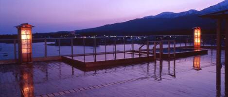 A wooden deck with a railing, two lit lanterns, and a view of mountains in the background.