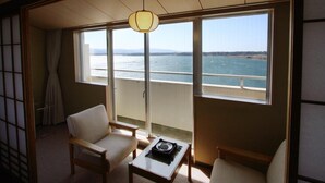 A room with a view of the sea, featuring two chairs, a small table, and a traditional Japanese sliding door. - Kohan no Yado Yoshidaya (Sado)