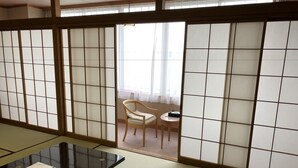 A traditional Japanese room with tatami flooring, a low table with menus, and a sliding door leading to a balcony with a chair and table. - Kohan no Yado Yoshidaya (Sado)