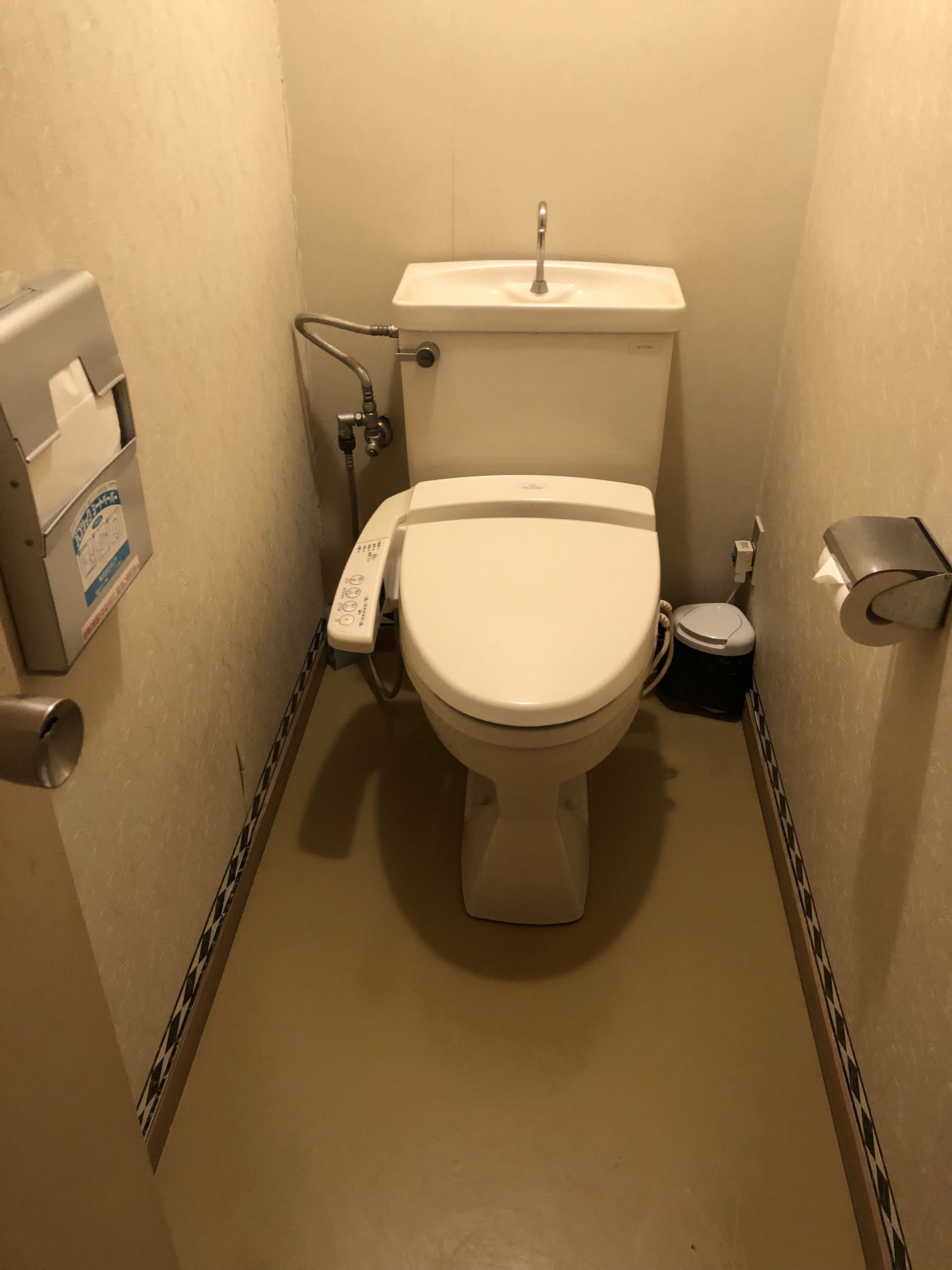 A small, compact bathroom with a toilet, a hand dryer, and a paper towel dispenser.