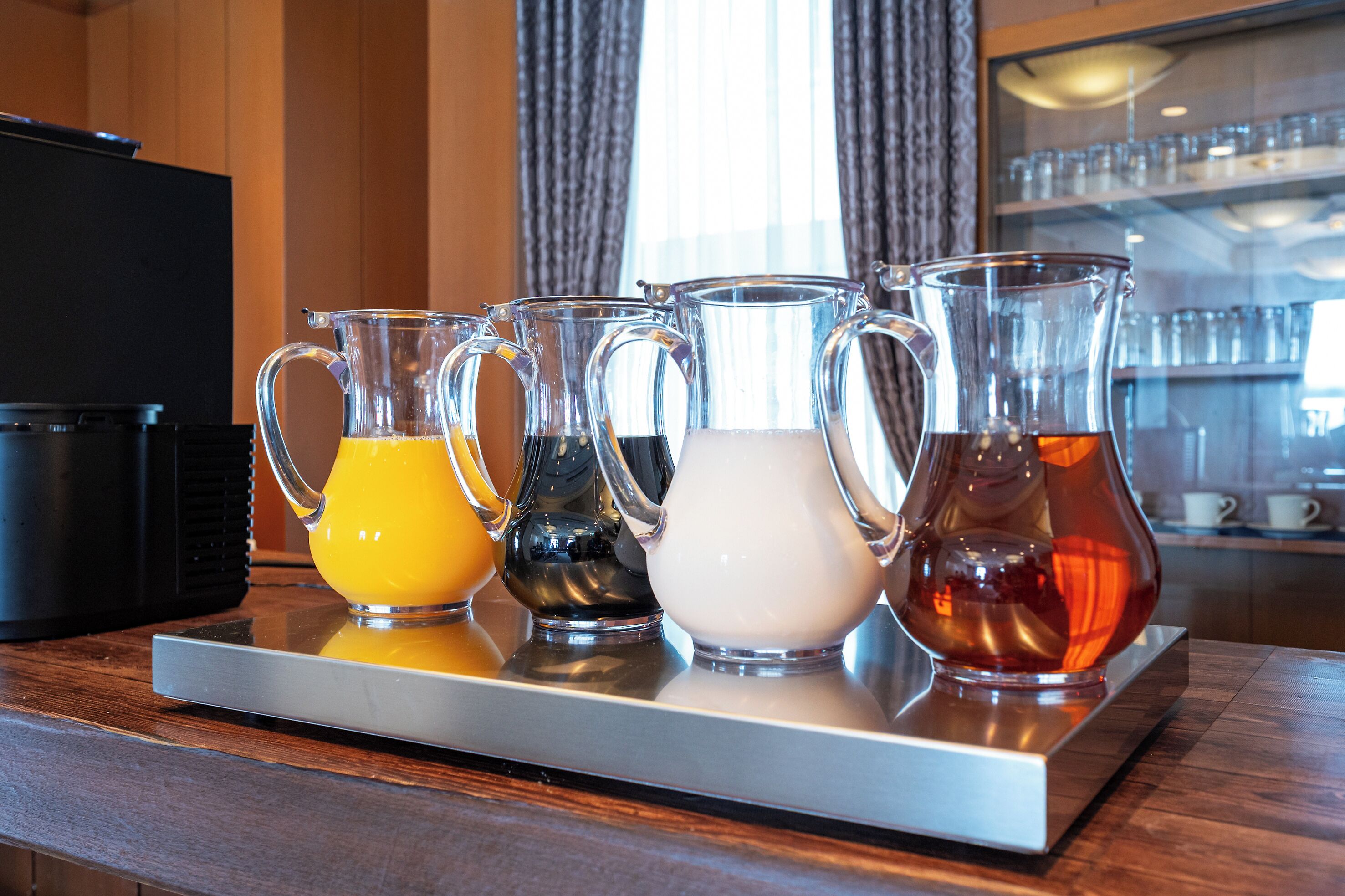 Un plateau contenant quatre carafes de différentes boissons, posé sur un comptoir en bois.