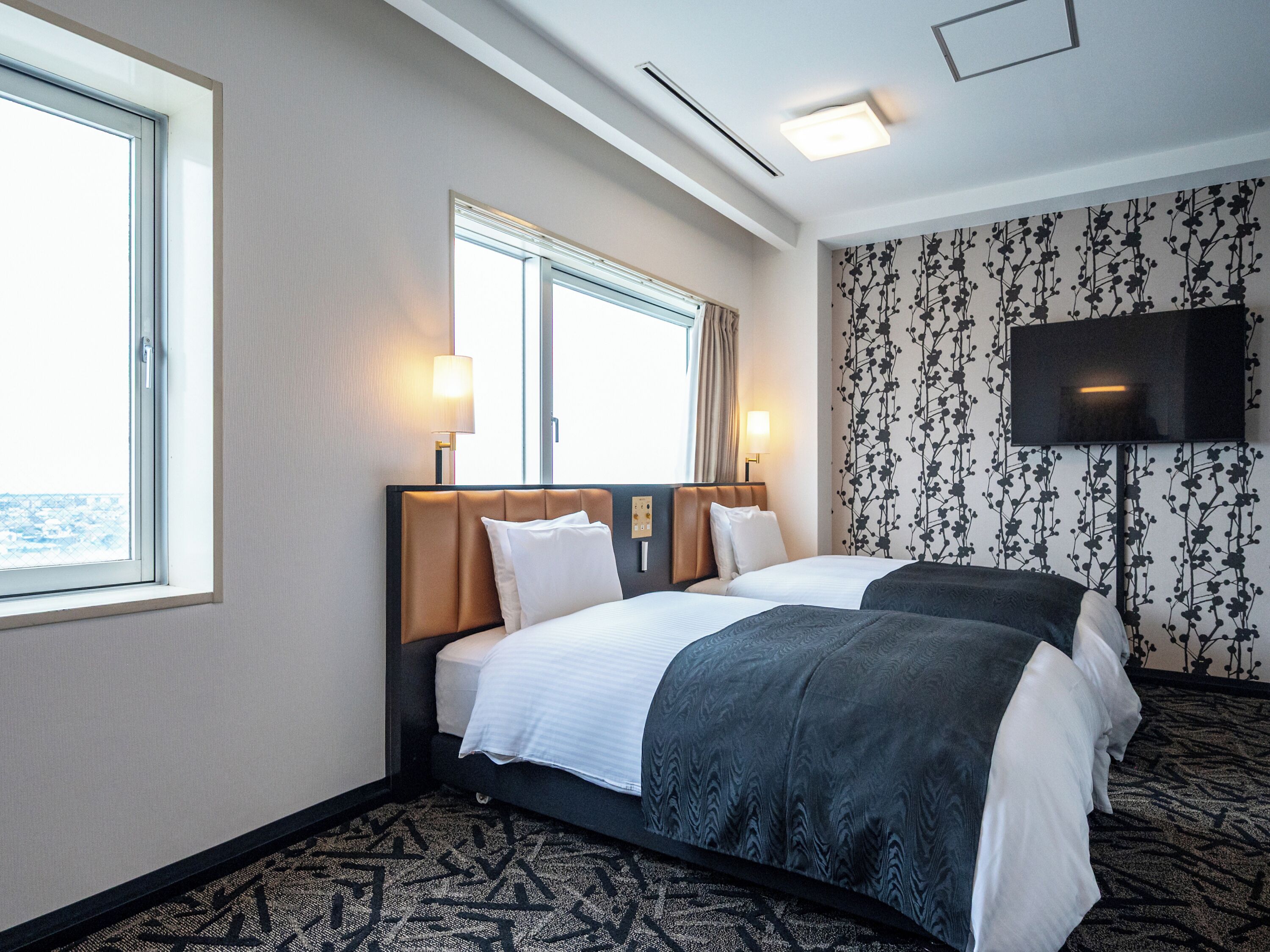 A hotel room with two beds, a TV, and a window with curtains.