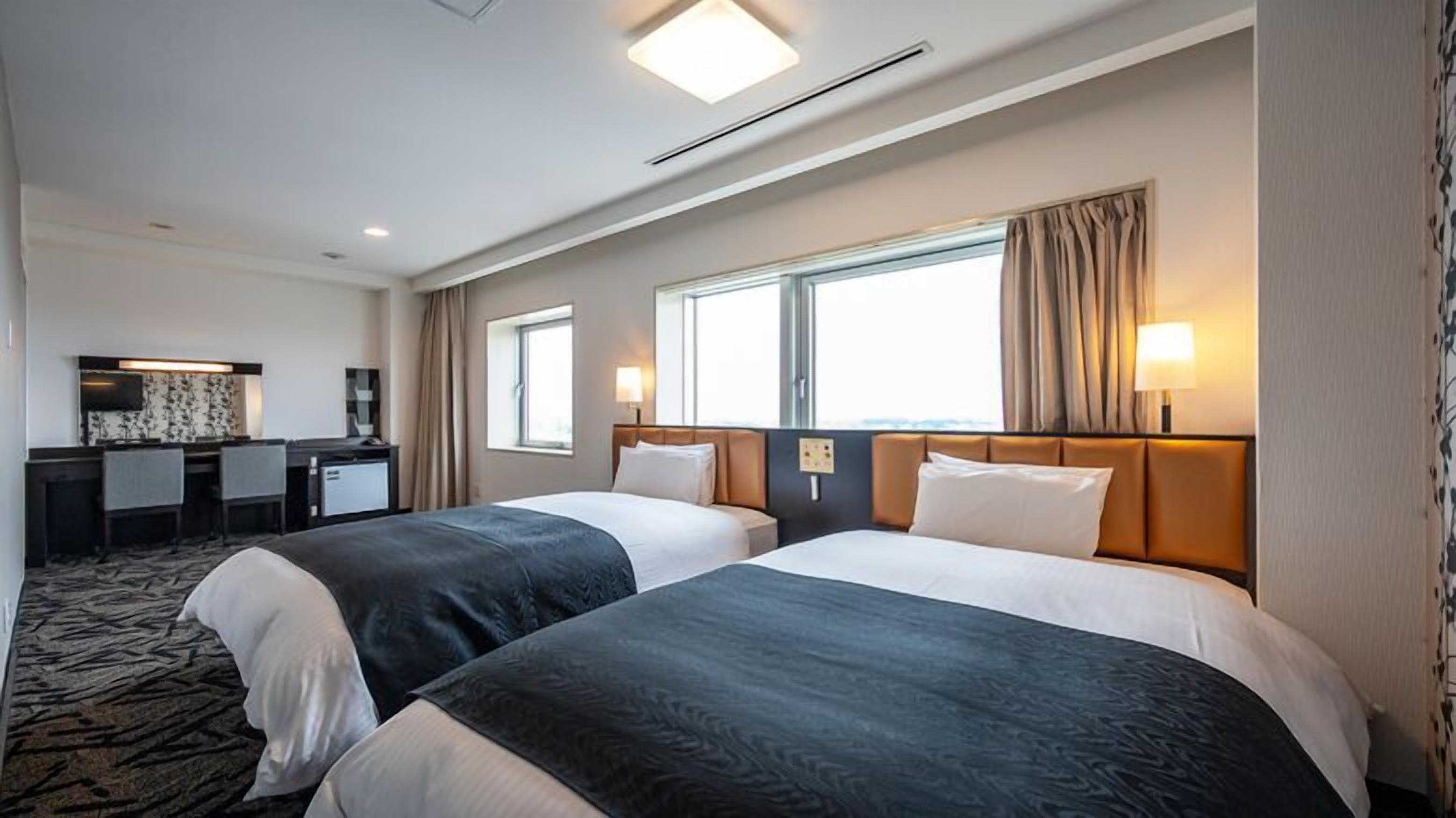 A hotel room with two beds, a desk, and a large window.