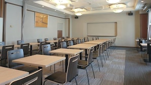 Una sala de conferencias con varias mesas y sillas, una pantalla de proyector y luces en el techo.