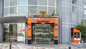 La entrada del APA HOTEL con fachada de vidrio, un letrero visible de cafetería restaurante y una vista despejada del área de acceso.