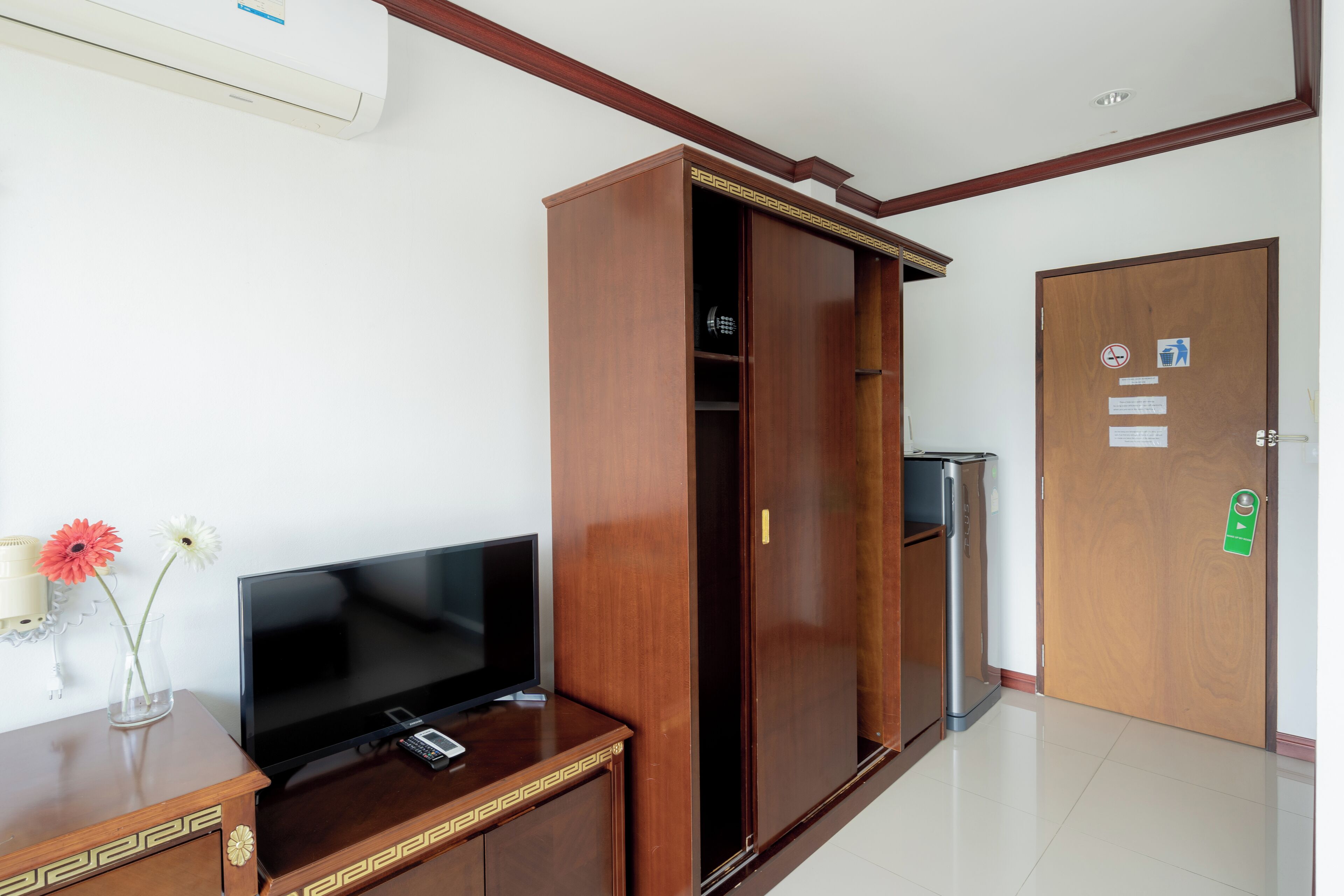 A room with a wooden wardrobe, a television on a wooden stand, a trash bin, and a door with a green handle.