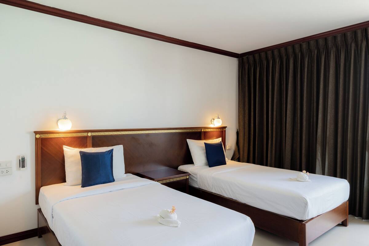 Habitación de hotel con dos camas individuales, cada una con una almohada y una mesita.