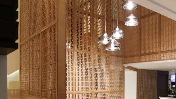 Un interior moderno con una escalera, un separador de madera y una zona de estar con iluminación colgante.