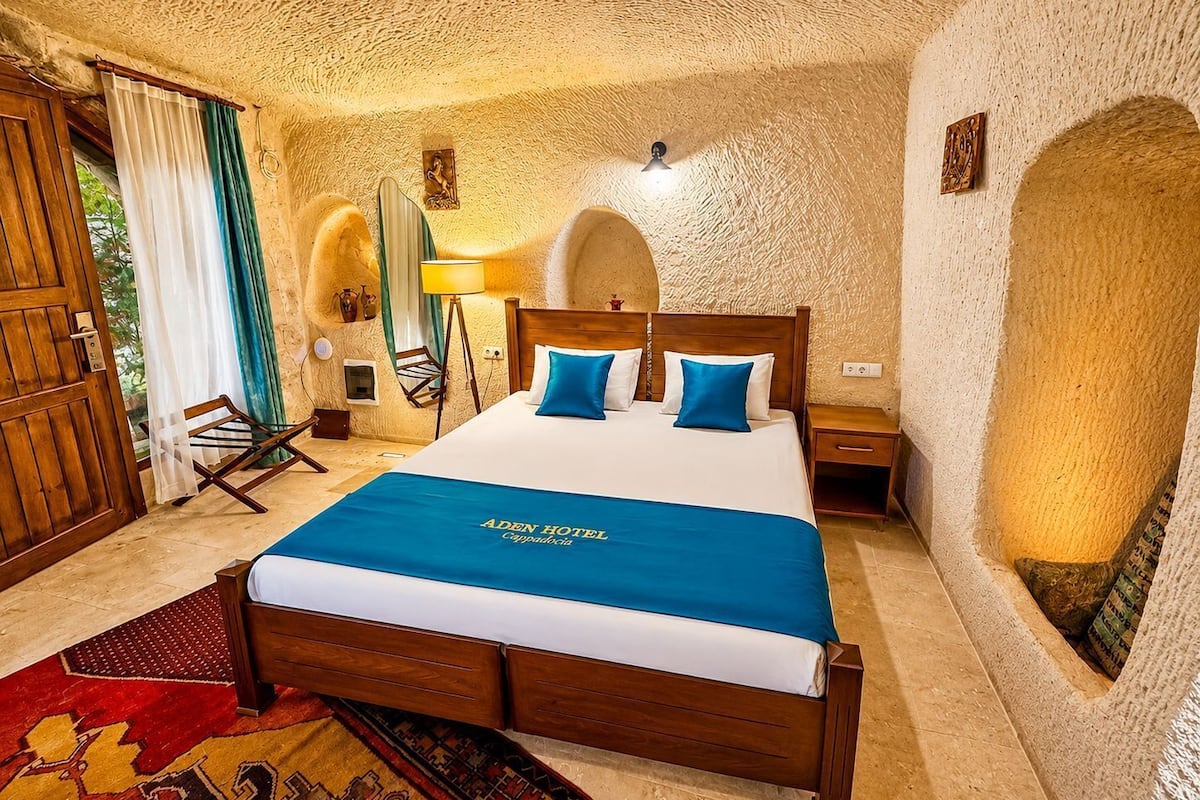 Quarto de hotel com cama de madeira, colcha azul e tapete vermelho estampado.