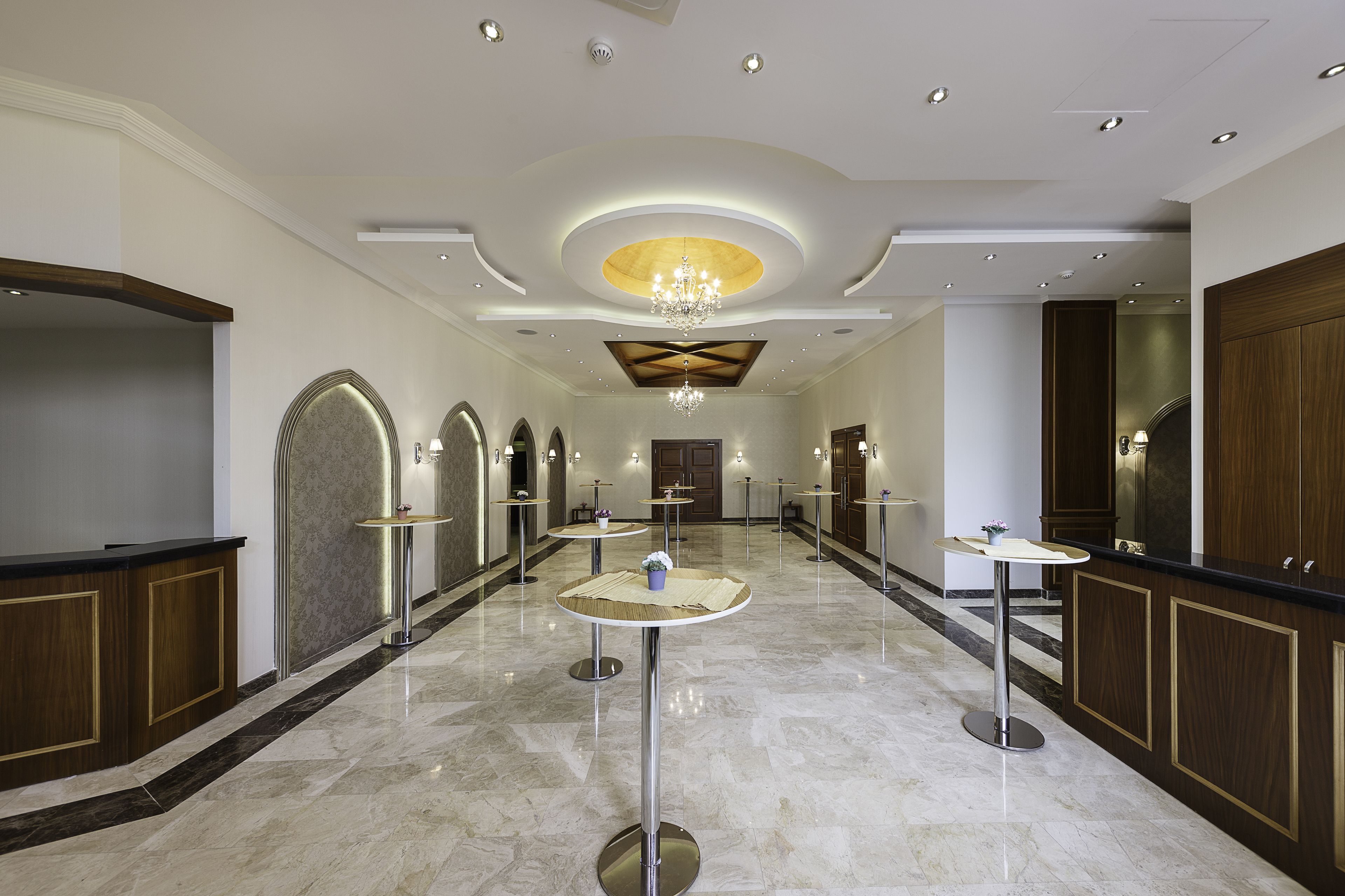 A hotel lobby with marble flooring, round tables, and a chandelier.