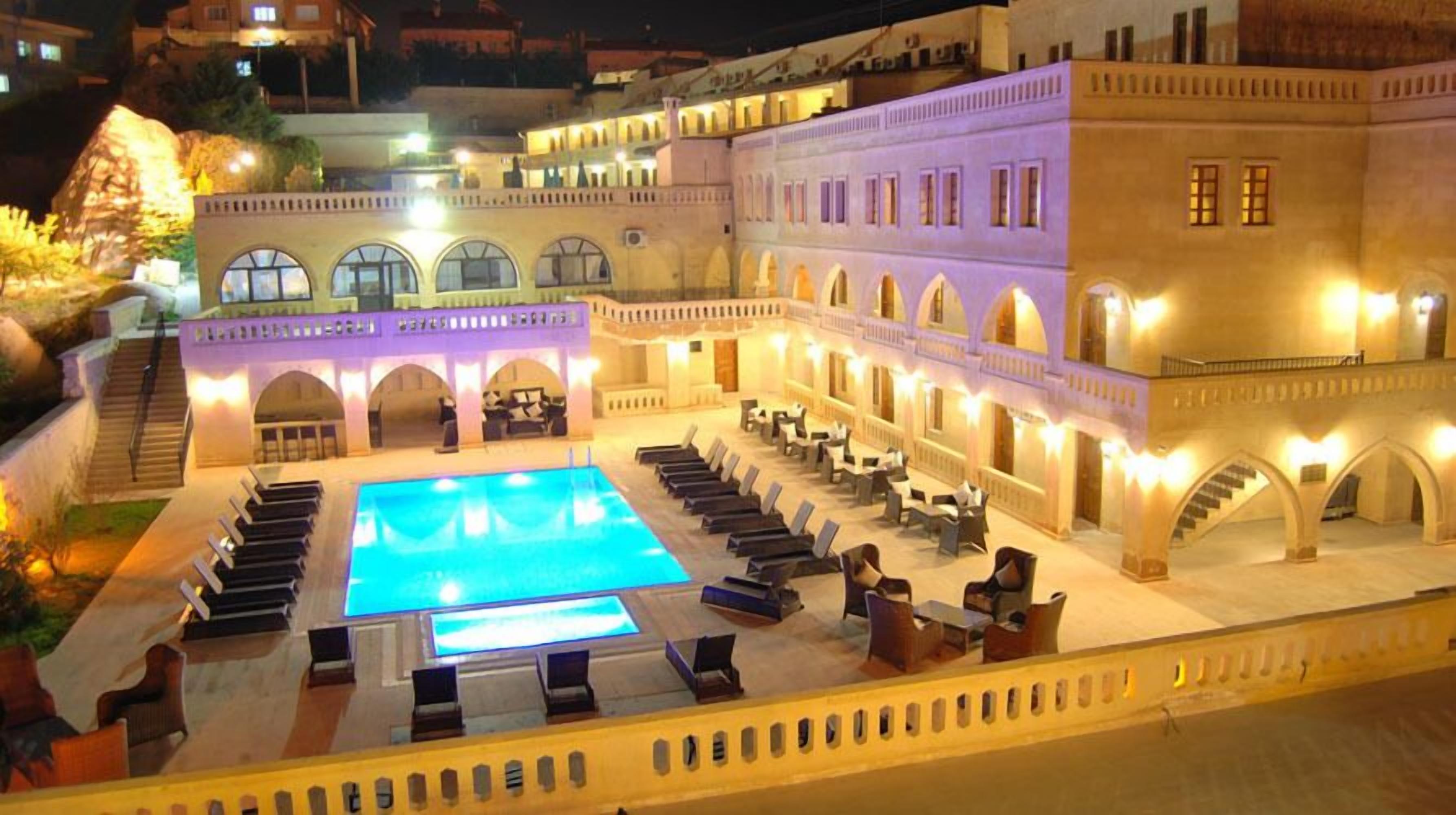 Un patio de hotel con piscina, tumbonas y una escalera que sube a los pisos superiores.