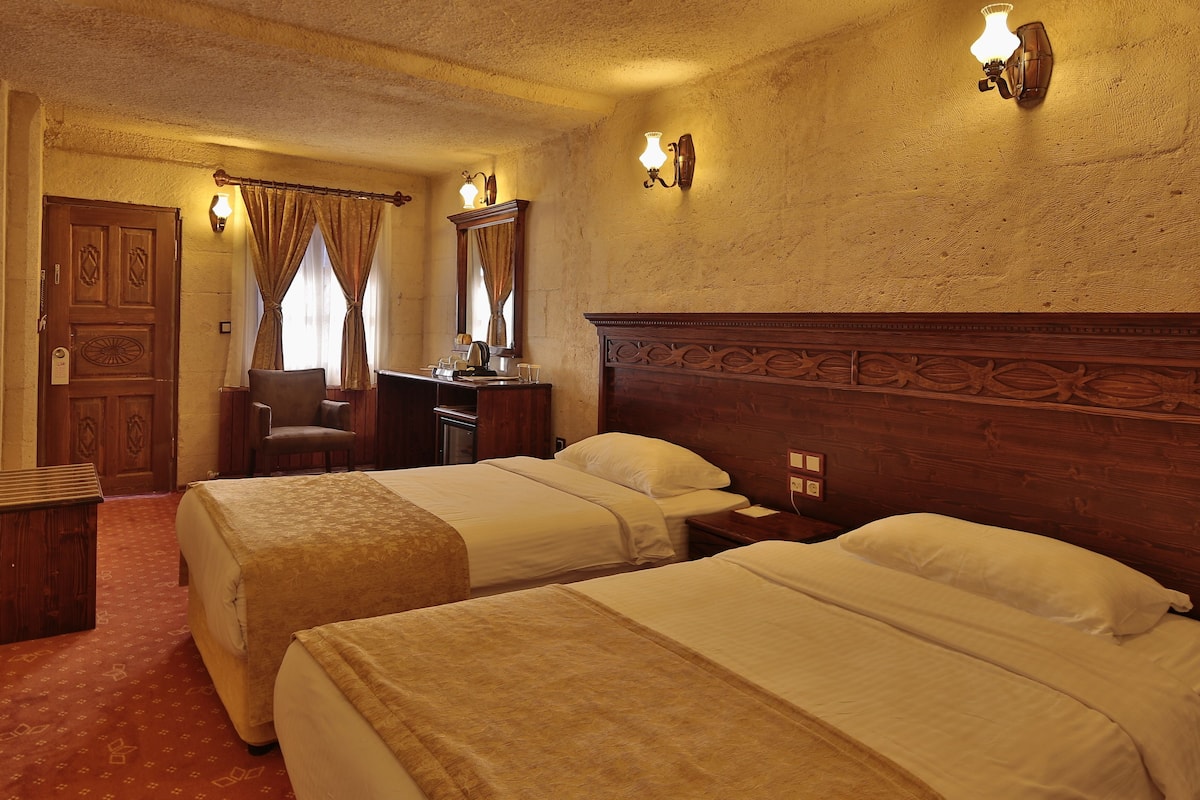 Quarto de hotel com duas camas, uma escrivaninha, uma cadeira e uma televisão.