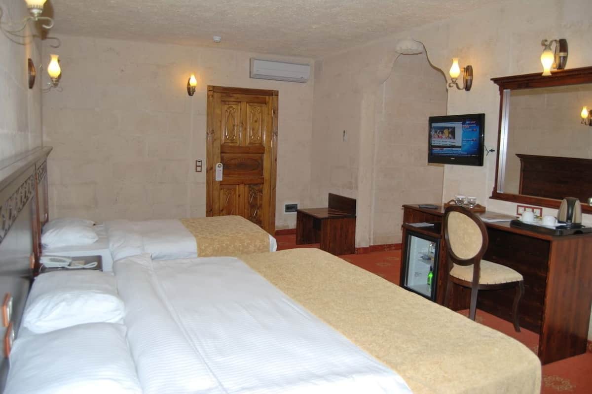 Quarto de hotel com duas camas, uma escrivaninha, uma cadeira, uma televisão e uma porta de madeira.