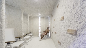 A room with white textured walls, a whiteboard, and a person sitting on a chair.