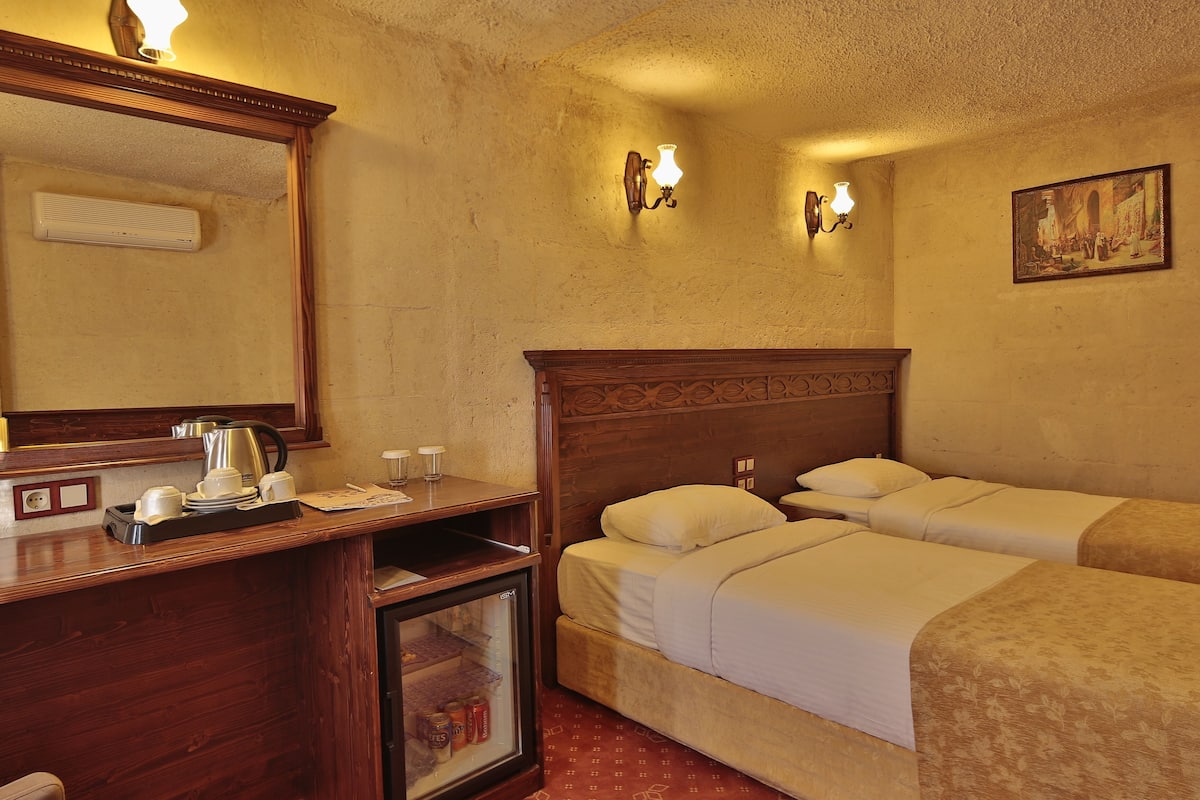 Quarto de hotel com cômoda de madeira, cama com duas almofadas, luminária na parede e uma pintura na parede.