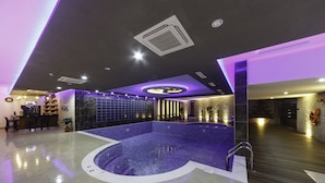 A modern indoor swimming pool with a unique geometric design, surrounded by a bar area and seating.