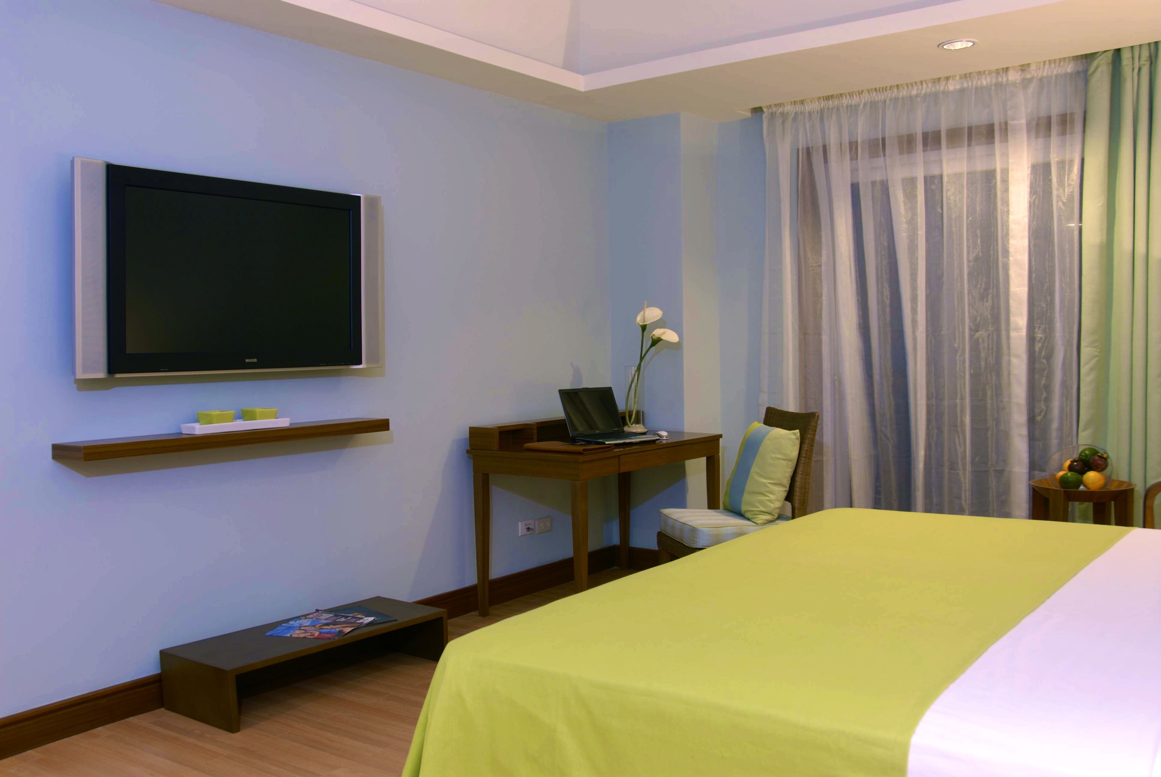 A hotel room with a bed, a desk with a laptop, a TV, and a window with curtains.