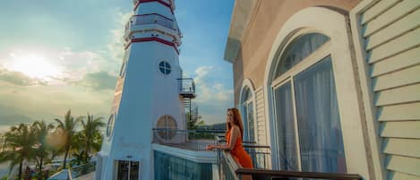A woman on a balcony overlooking a white building with a red and blue lighthouse.