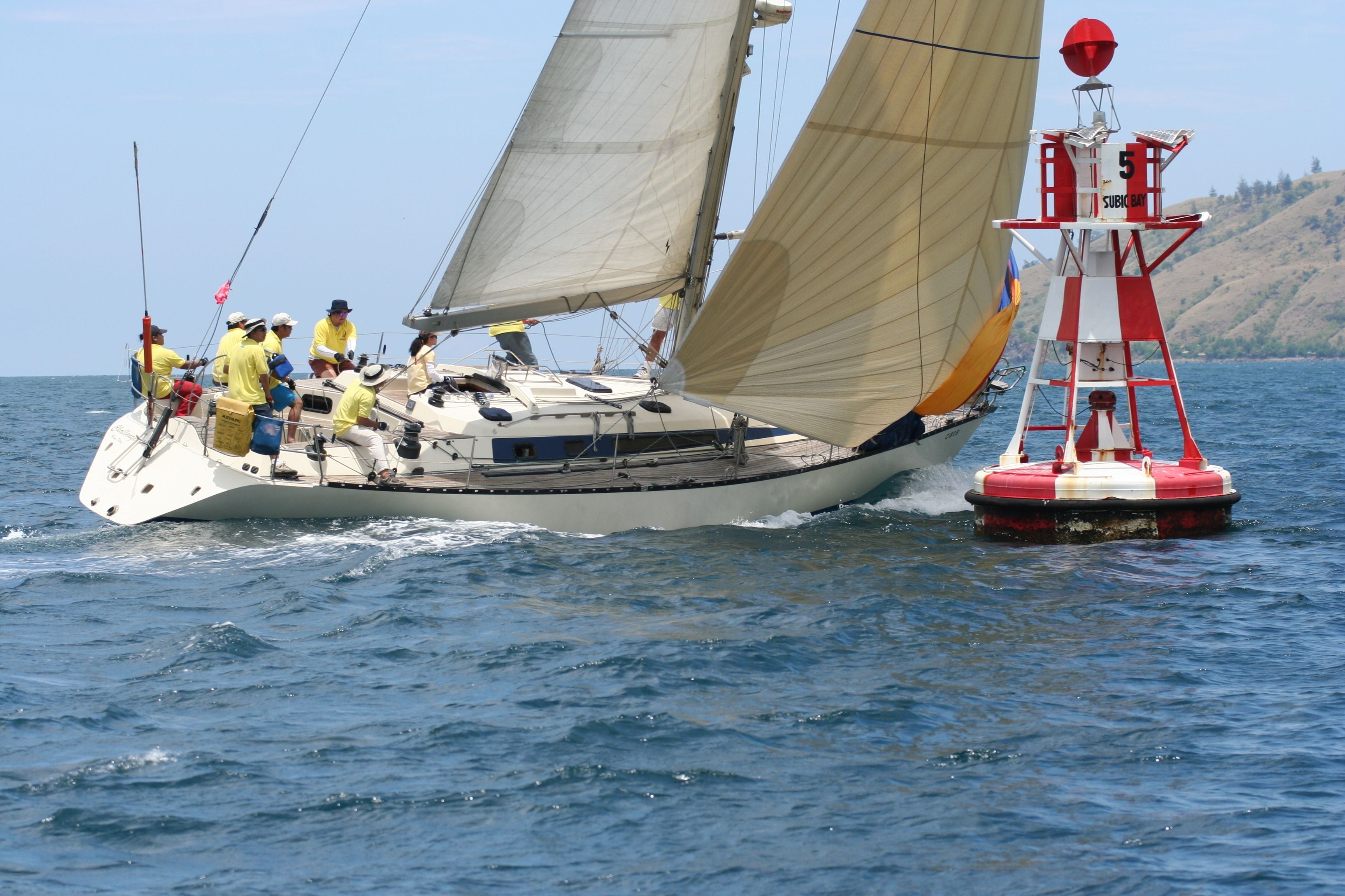 A sailboat with multiple people on deck, a lifebuoy, and a buoy in the water.