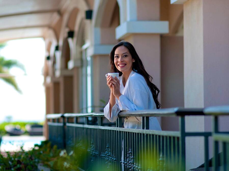A person standing on a balcony with a railing, holding a cup.