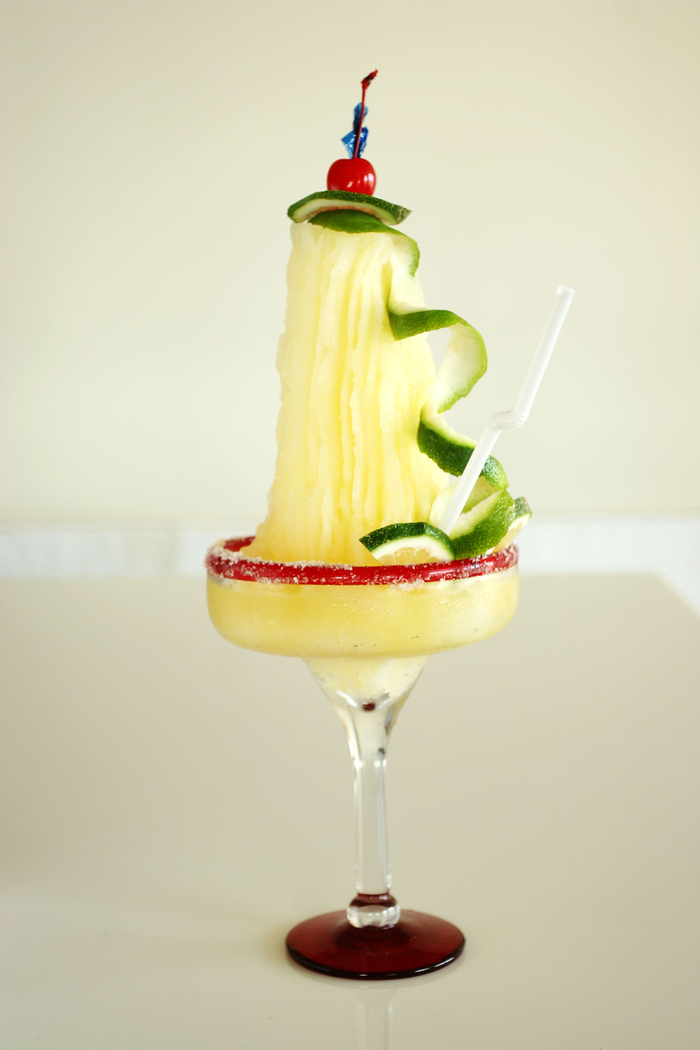 A cocktail in a glass with a red rim, garnished with lime and a cherry.