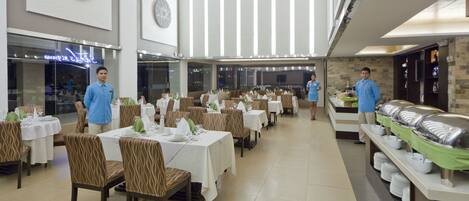 A spacious dining area with multiple tables and chairs, a buffet line, and a large clock on the wall.