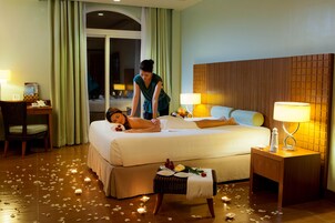 Habitación de hotel con cama, dos lámparas de noche, una mesita con una vela y una silla.