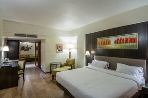 Habitación de hotel con una cama grande, un escritorio, una silla, una mesita y un cuadro en la pared.