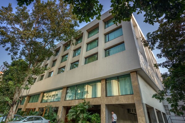 Un edificio moderno con varios pisos, ventanas amplias y un árbol en primer plano.