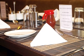 Mesa de comedor de hotel dispuesta con platos, cubiertos y un atril para el menú.