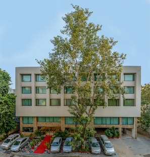 Un edificio de varios pisos con un árbol central, una alfombra roja y varios coches estacionados.