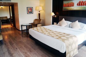 A hotel room with a large bed, two bedside lamps, a small table, a chair, and a painting on the wall. - The President - A Boutique Hotel (Ahmedabad)