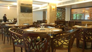 A restaurant with round tables and wooden chairs, a TV mounted on the wall, and a person in the background.