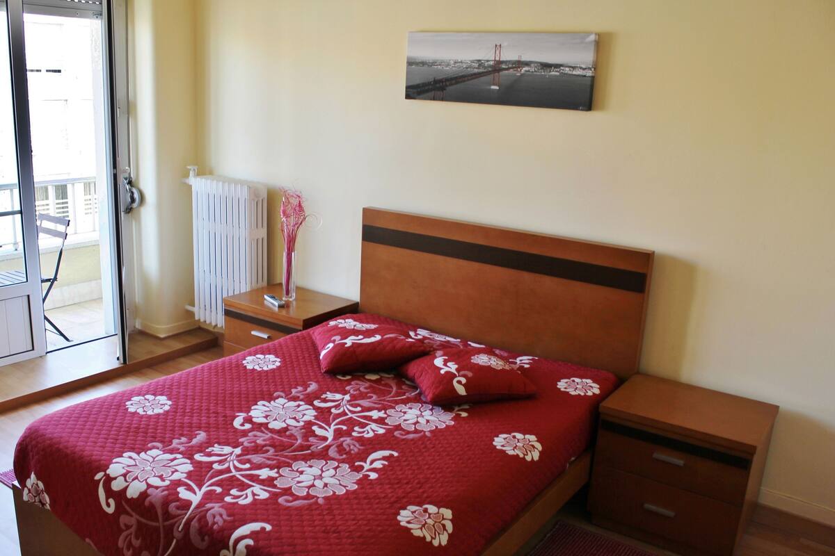 A bedroom with a bed, a nightstand, a drawer, a radiator, a window, and a picture on the wall.