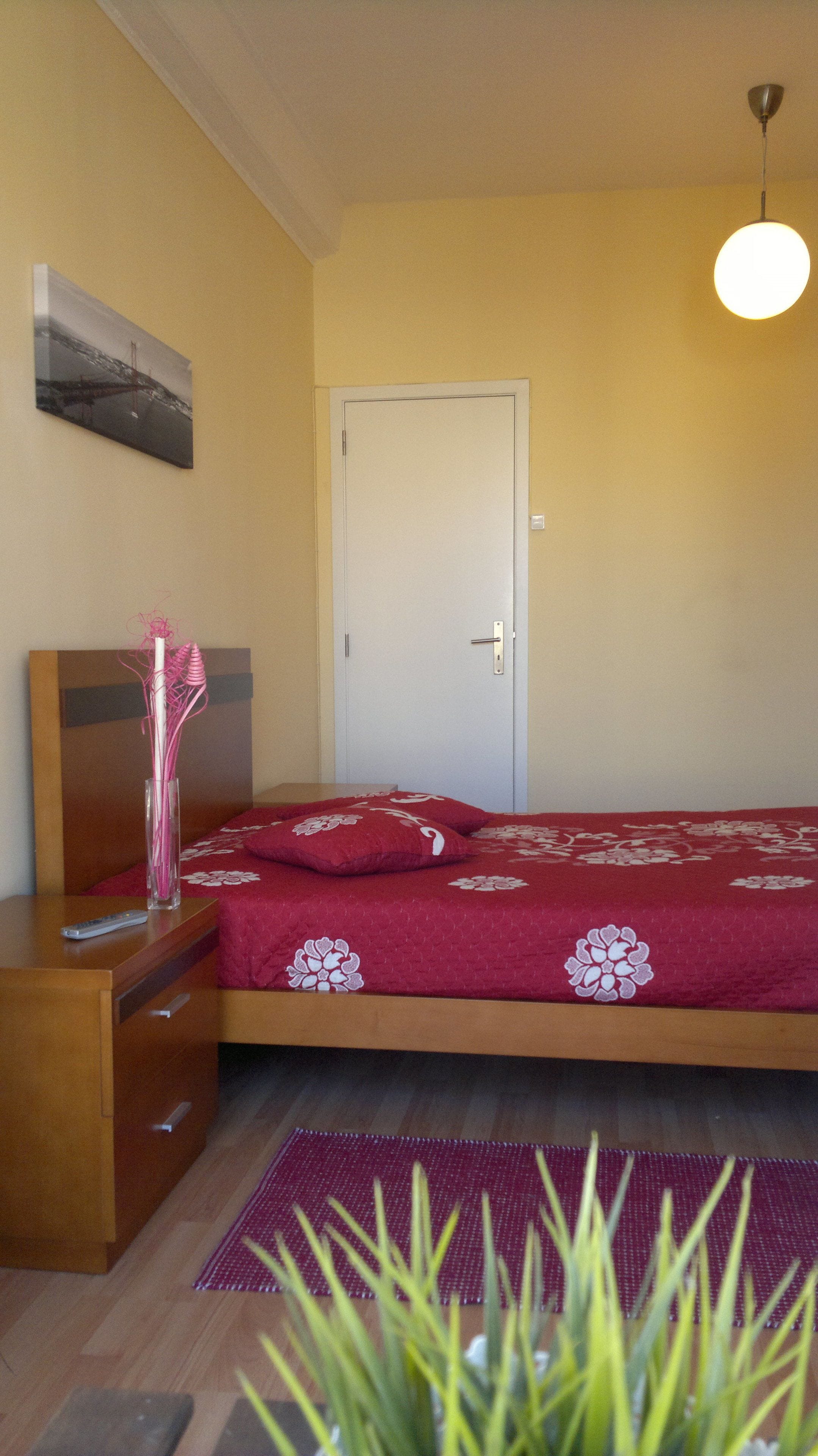 Une chambre à coucher avec un lit, une commode en bois, une porte et un luminaire suspendu.