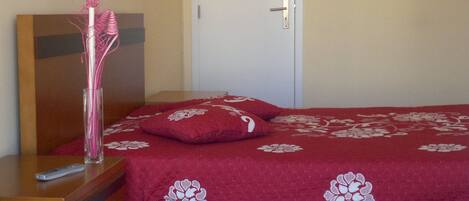 A bedroom with a bed, a wooden dresser, a door, and a hanging light fixture.