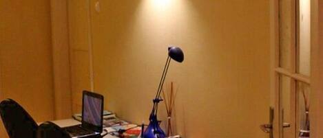 Una habitación con un escritorio, una silla, una computadora portátil, una lámpara y una puerta con paneles de vidrio.