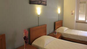 A hotel room with two single beds, a nightstand with a lamp, a decorative vase, and a painting of a bridge on the wall. - Residencial Duque de Saldanha (Lisbon)