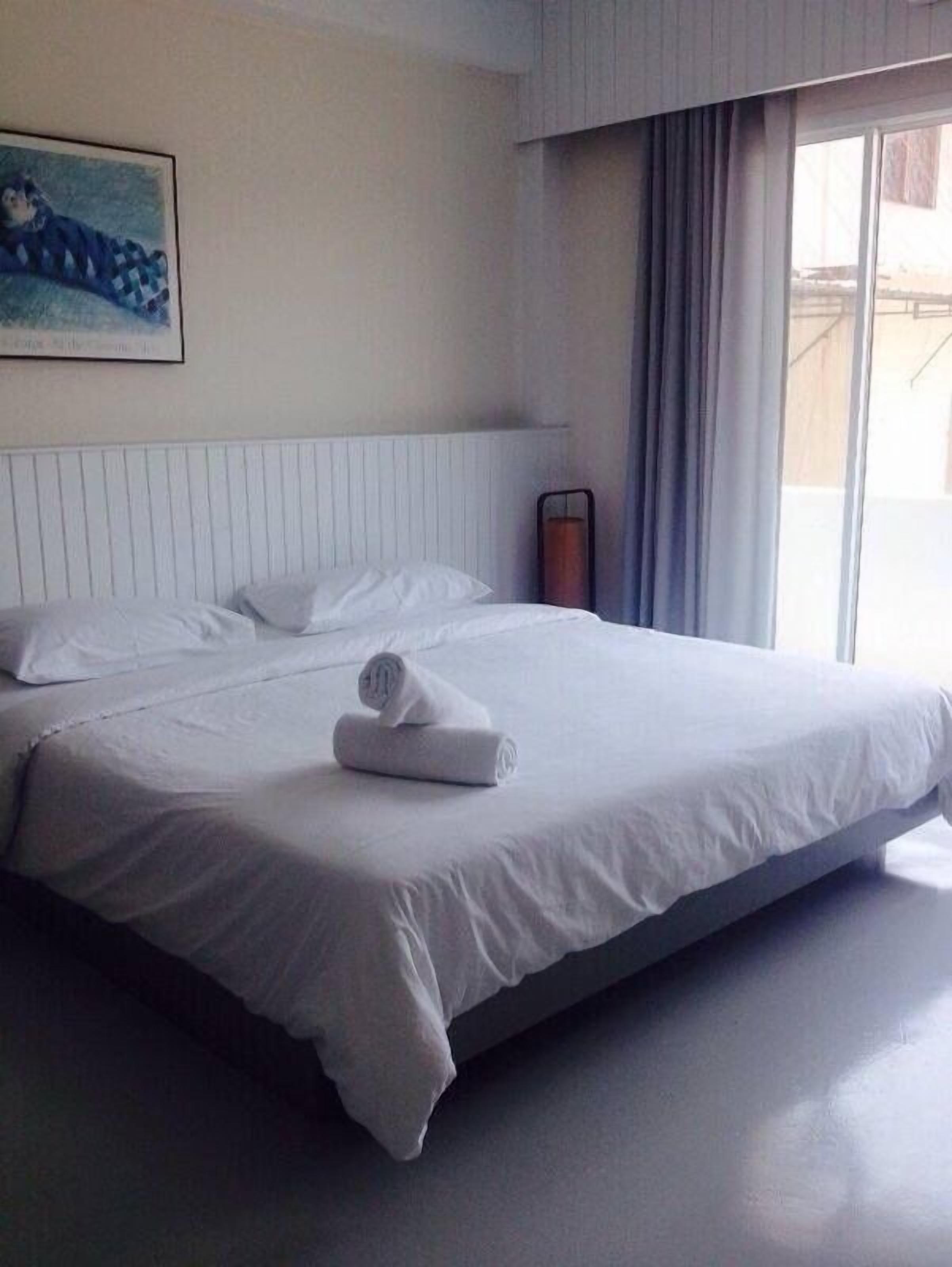 A hotel room with a large bed, white bedding, a painting on the wall, and a window with curtains.