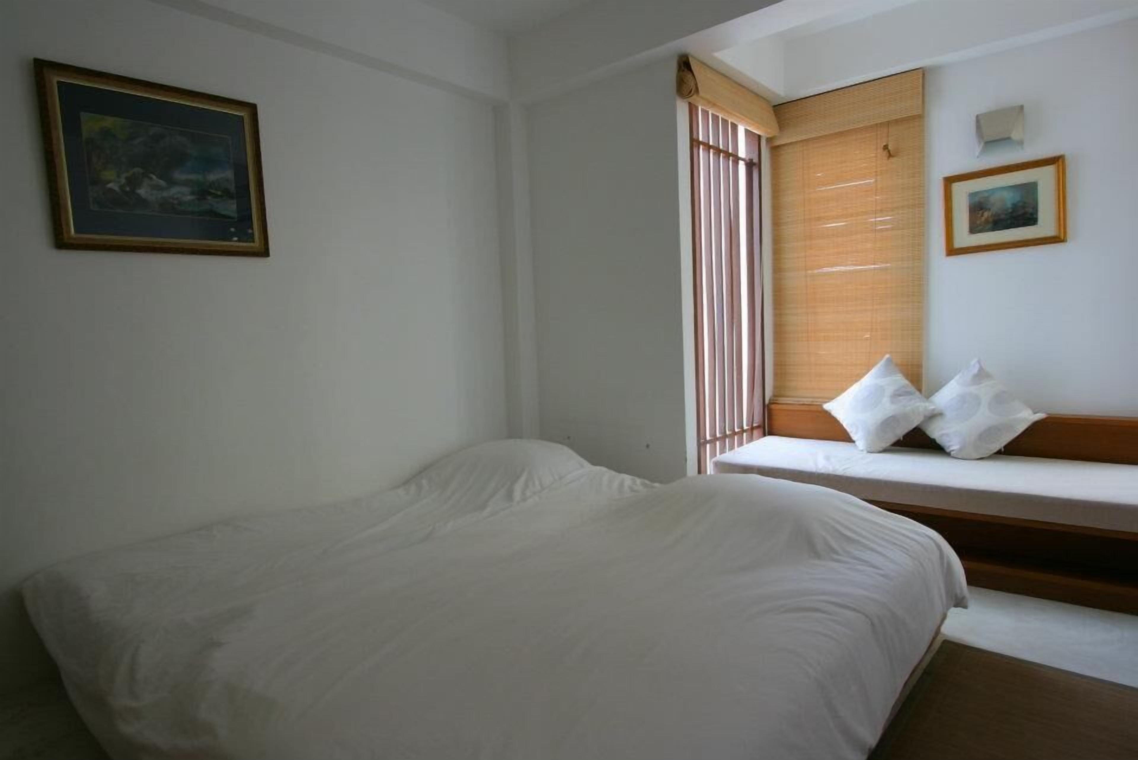 Quarto com cama, janela com persianas e quadro pendurado na parede.