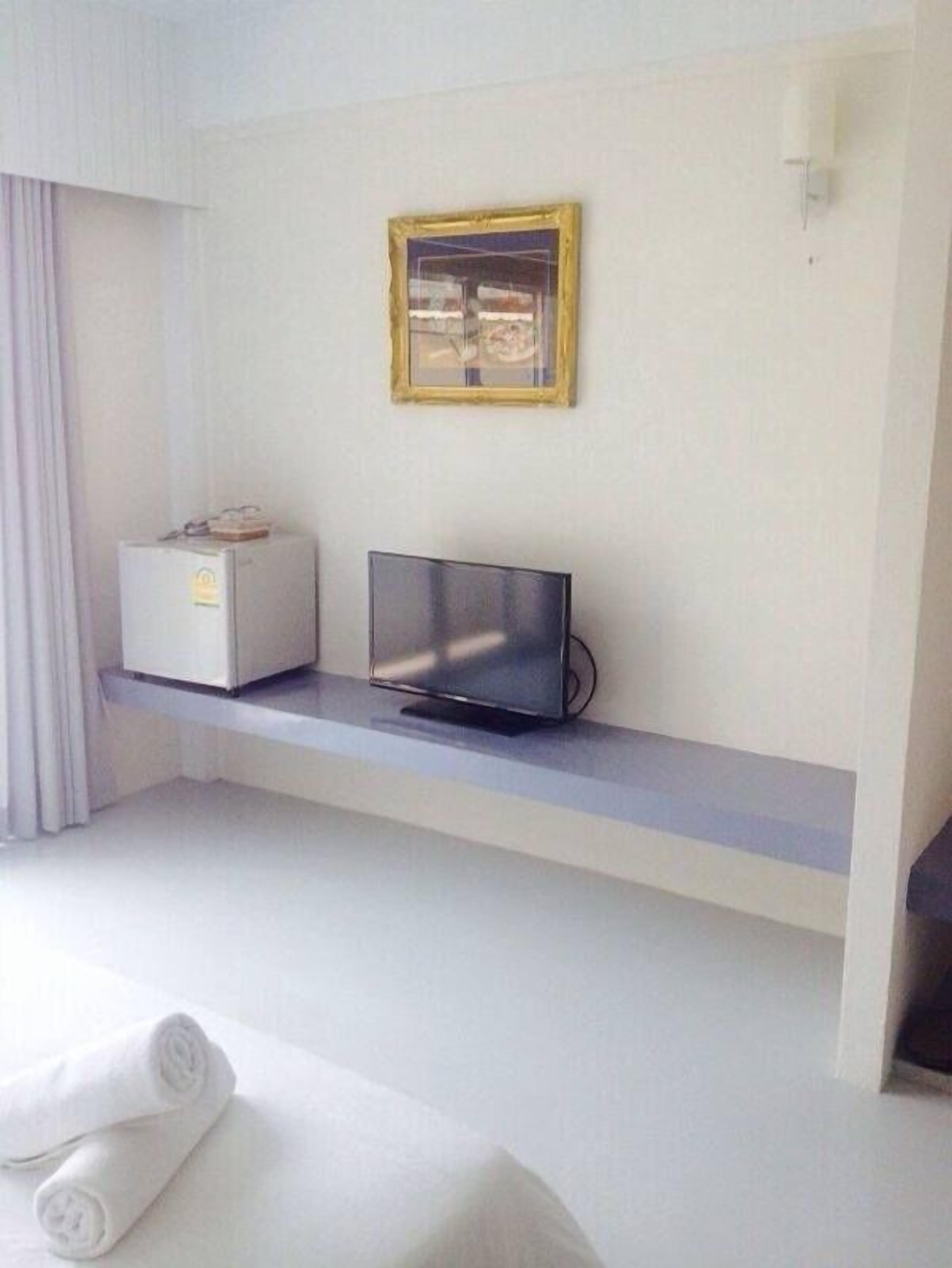 Une chambre d’hôtel avec un lit, un téléviseur posé sur une étagère, un petit réfrigérateur et un tableau encadré au mur.