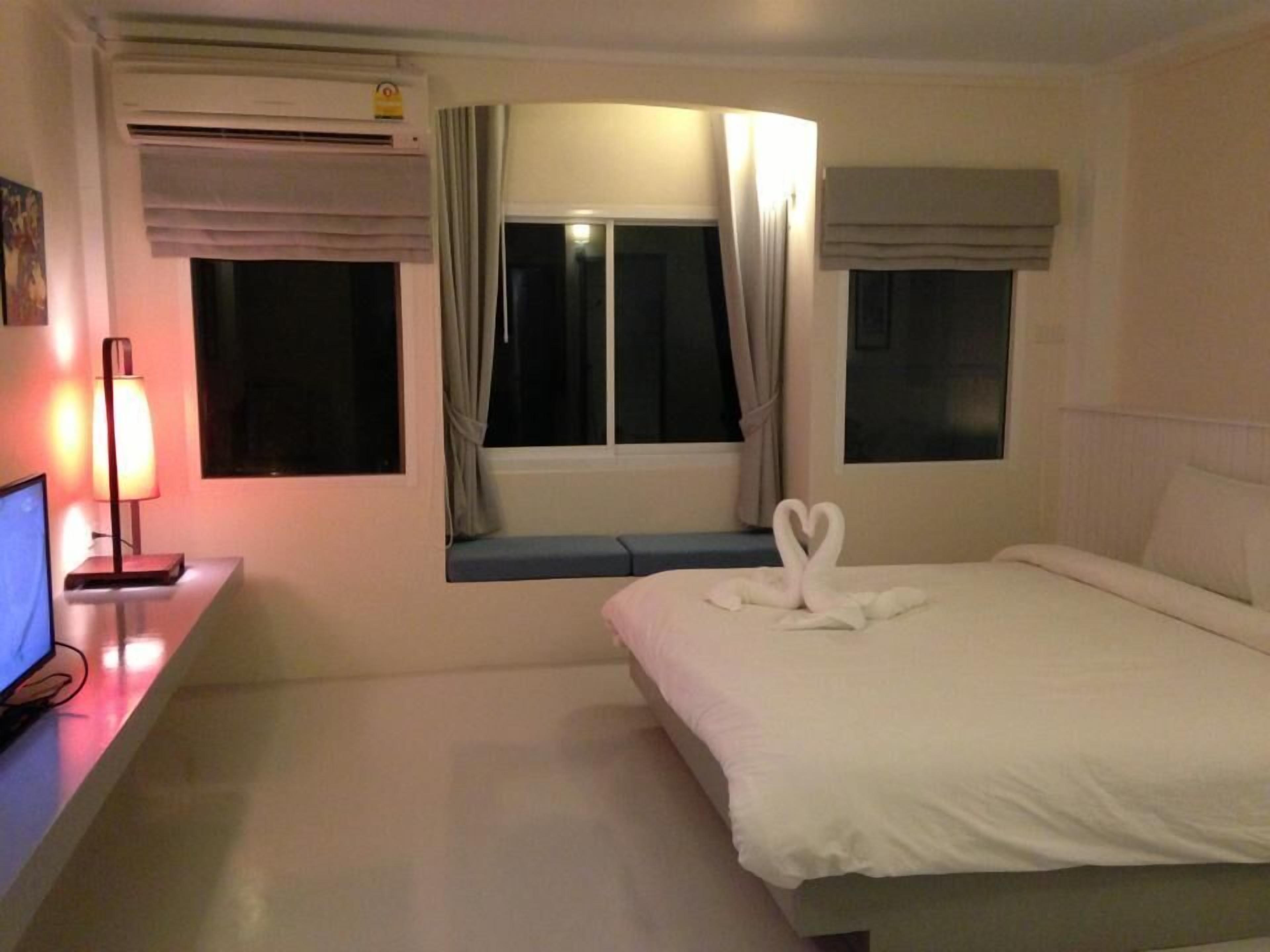 A hotel room with a bed, a desk with a computer, an air conditioner, and a window with curtains.