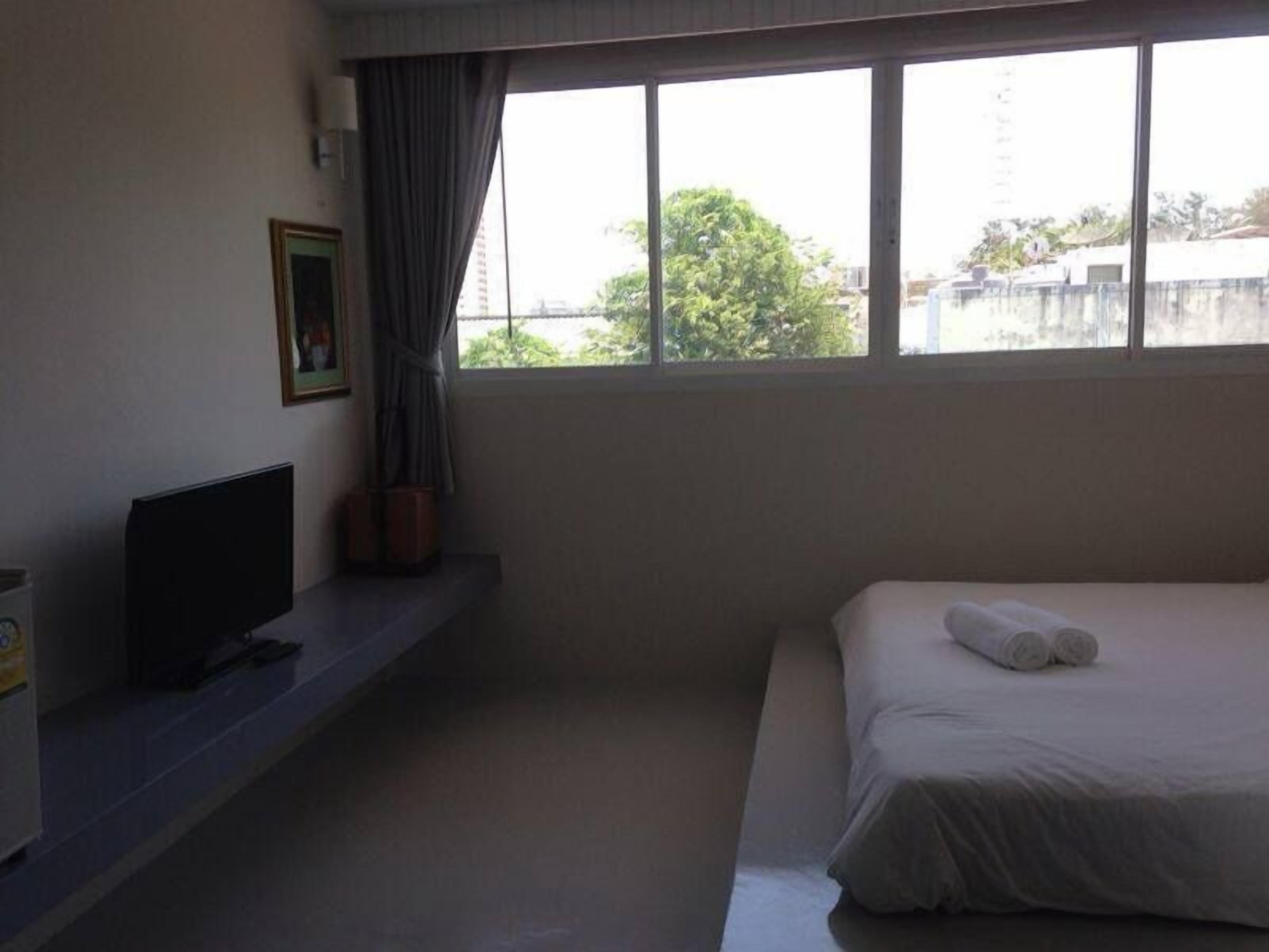 Habitación de hotel con cama, televisor sobre un mueble, ventana con cortinas y una mesita con una planta.