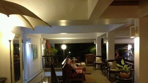 Een ruime binnenzone met een trap die naar een balkon leidt. Er staan meerdere stoelen en een bank, geordend voor zitplaatsen. Een grote vaas is rechts zichtbaar.