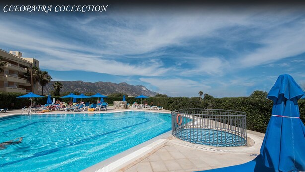 A pool area with lounge chairs and umbrellas, surrounded by mountains and a clear sky. - Cleopatra Superior (Kos)