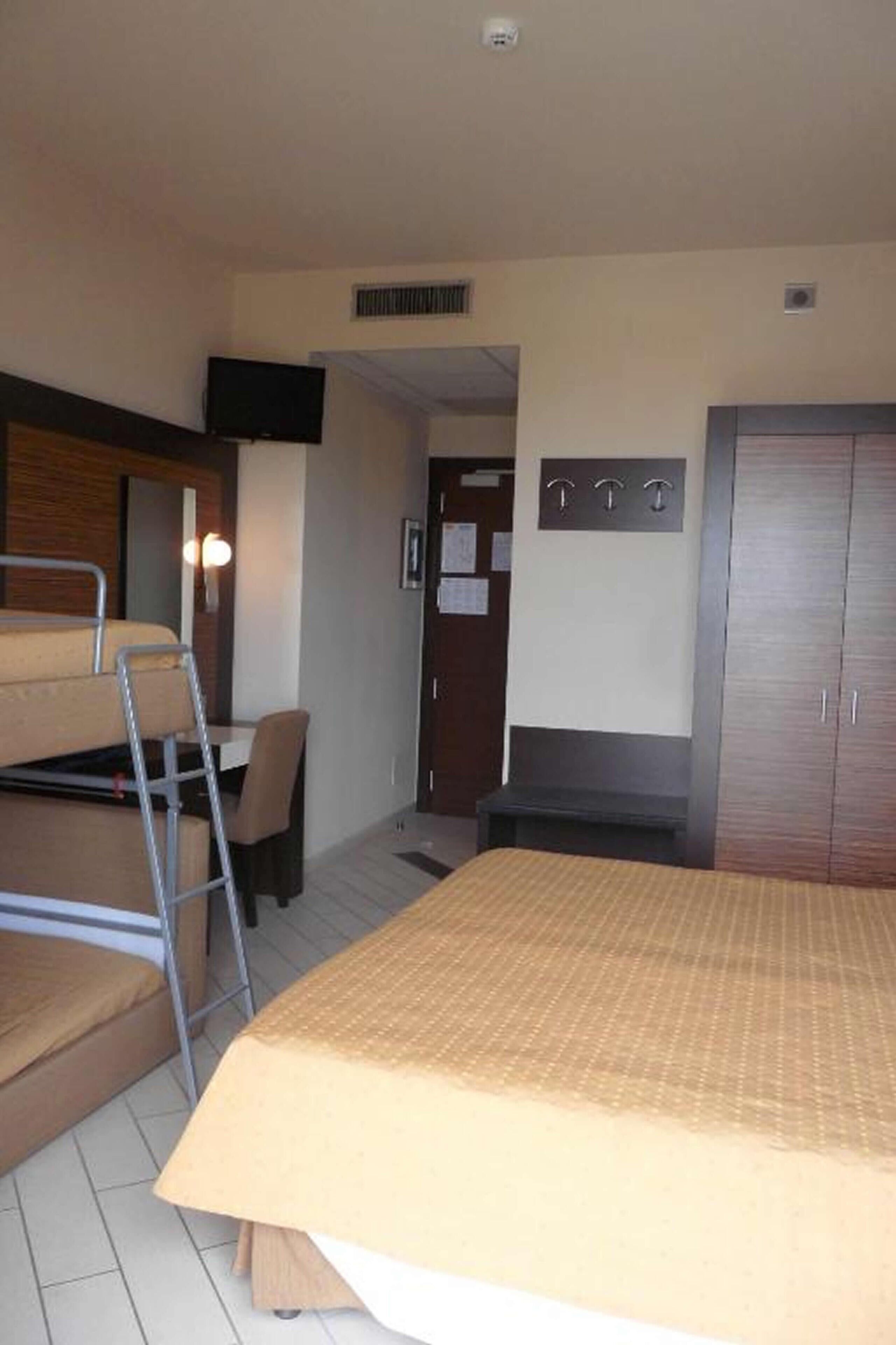 A room with bunk beds, a desk, a chair, a wardrobe, and a TV.