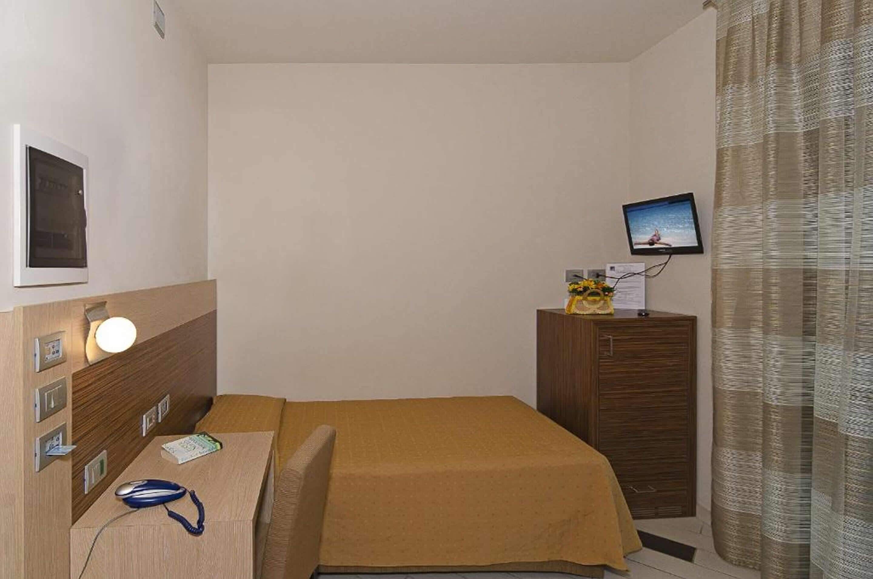 Habitación de hotel con cama, escritorio con computadora, televisor en un mueble y cortina.